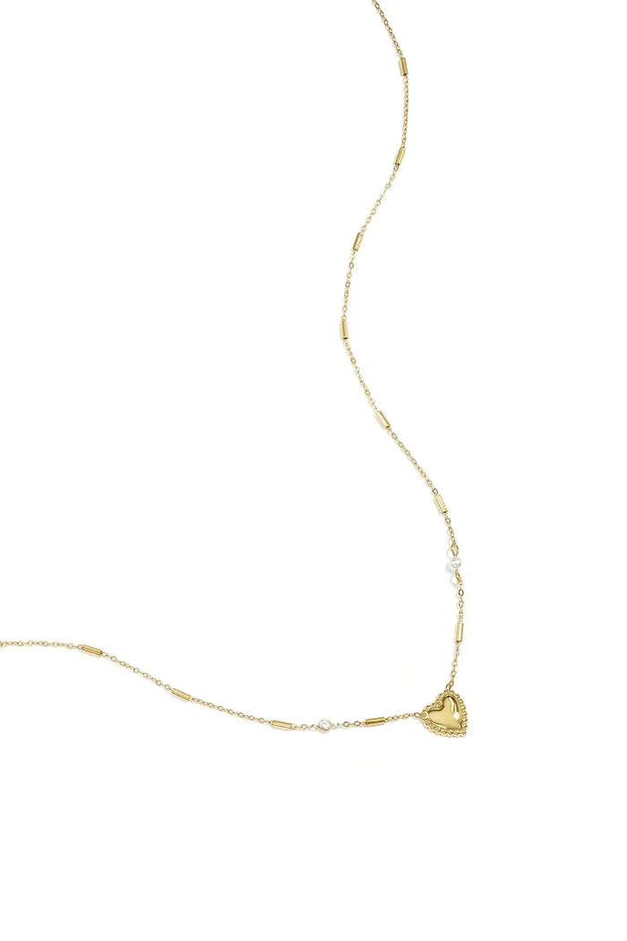 A gold-plated stainless steel chain necklace featuring a central beaded-border heart pendant, cylindrical bar links, a small clear cubic zirconia stone, and a tiny pearl accent. adore-beaded-heart-station-necklace.webp