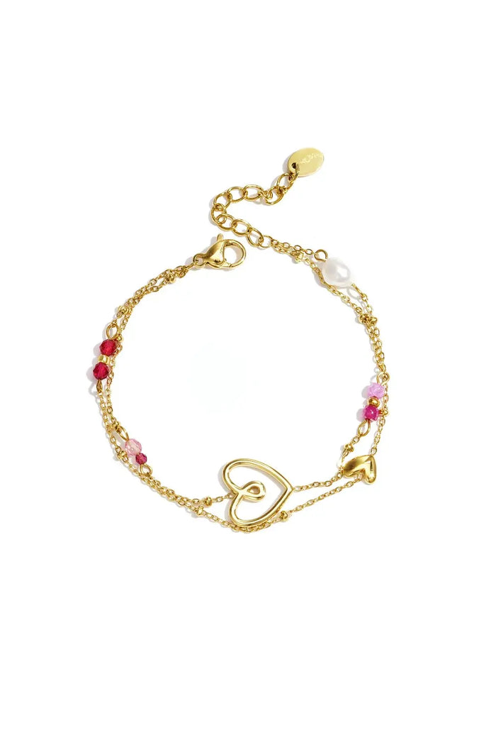 A double-strand gold-plated stainless steel bracelet featuring an open heart centerpiece, a puffed heart charm, a white freshwater pearl, and pink and red crystal beads against a white background. amara-open-heart-pearl-layered-charm-bracelet.webp