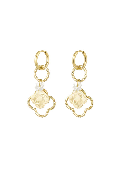 A pair of gold-plated stainless steel huggie hoop earrings featuring a cascading drop of a twisted ring, a tiny white mother of pearl clover, a central gold sunburst clover medallion, and a larger beaded open clover frame against a white background. aurelia-sunburst-clover-drop-huggie-earrings.webp