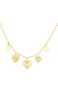 A gold-plated charm necklace featuring an oval link chain adorned with five different dangling heart charms, including a central 3D puffy heart, a sacred heart with a pink center, a textured sunburst heart with a crystal, and two small flat heart tags. cherie-amour-multi-heart-charm-necklace.webp