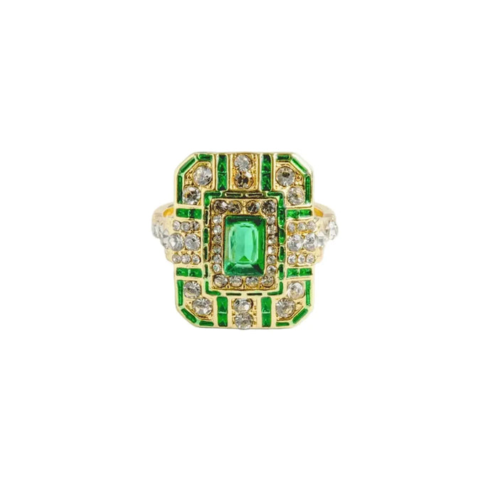 An ornate 14ct gold-plated Art Deco cocktail ring featuring a large rectangular emerald crystal centered on a geometric shield with green enamel and clear crystals.