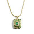 An ornate 14ct gold-plated Art Deco pendant necklace featuring a rectangular emerald crystal centered on a geometric shield with green enamel and clear crystals.