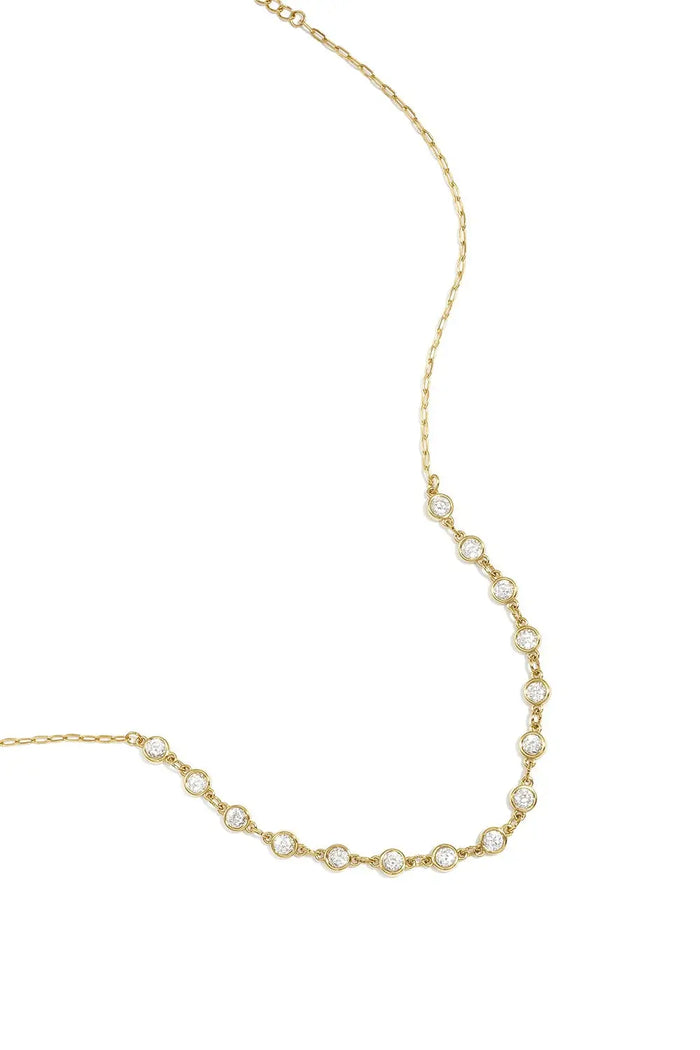 A gold-plated stainless steel necklace featuring a central arc of round cubic zirconia crystal stations connected to a fine link chain against a white background. clara-crystal-station-necklace.webp