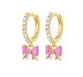 A pair of gold-plated 925 sterling silver huggie hoop earrings lined with clear pavé crystals and suspending a hand-painted bubblegum pink enamel bow charm.