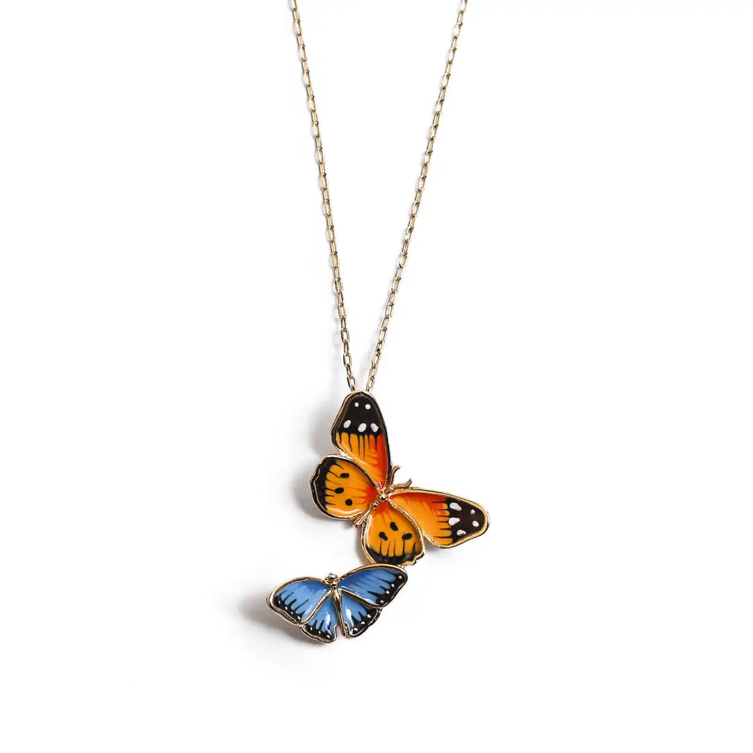 A gold-plated pendant necklace by Bill Skinner featuring a stacked design of two hand-painted enamel butterflies—one large orange monarch and one small blue butterfly. bill-skinner-dual-butterfly-necklace.webp