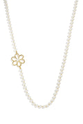 A strand necklace made of white glass pearls with an asymmetrical openwork gold flower charm featuring a center pearl against a white background. evangeline-asymmetric-floral-pearl-necklace.webp