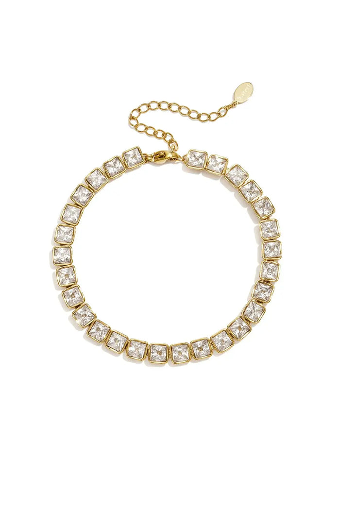 A gold-plated stainless steel tennis bracelet featuring a continuous strand of large square princess-cut cubic zirconia crystals with a lobster clasp and extender chain against a white background. evelyn-princess-cut-crystal-tennis-bracelet.webp