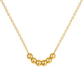 A gold necklace featuring seven polished gold beads arranged in a curve on a dainty cable chain, shown on a white background.