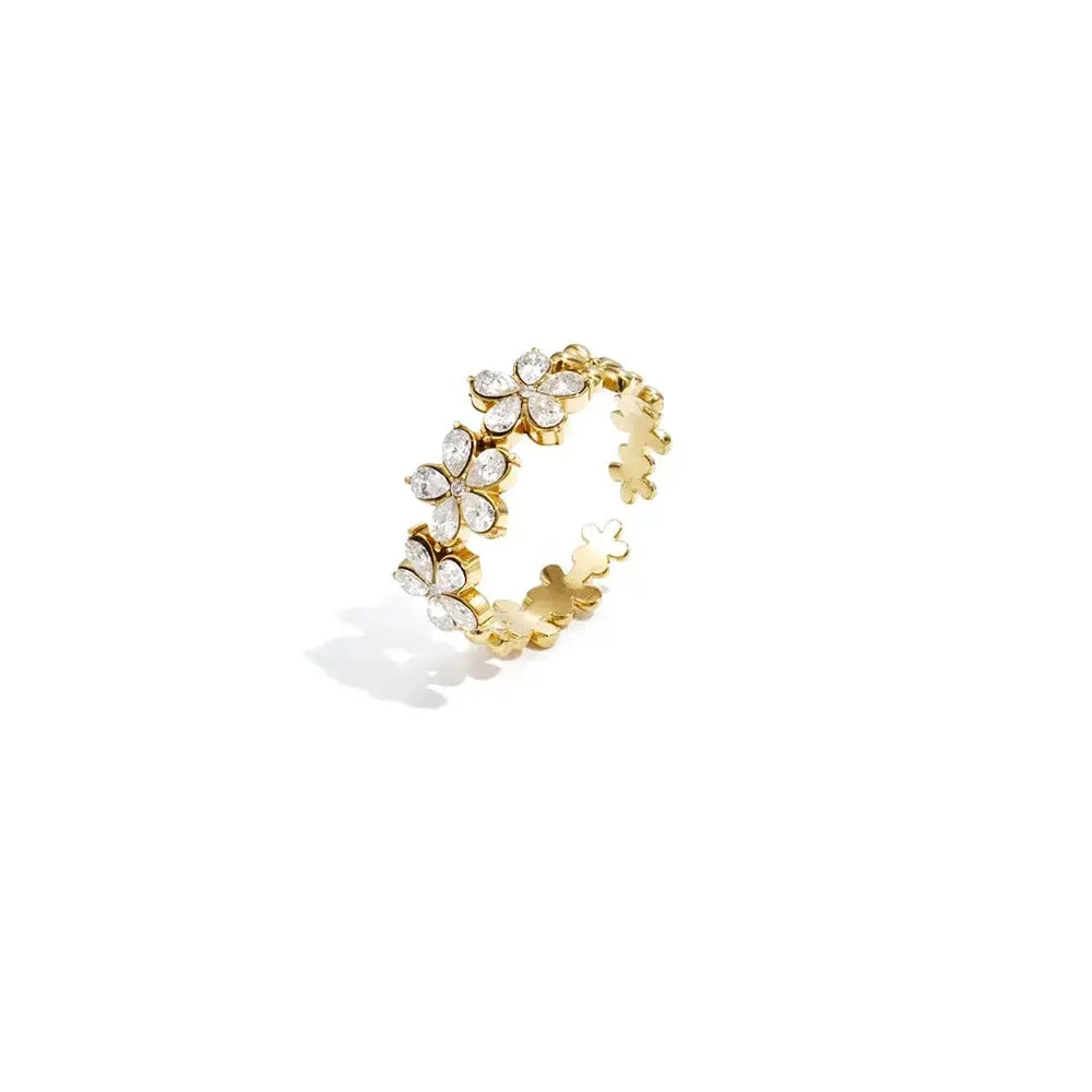 A gold-plated stainless steel adjustable ring featuring a front cluster of three clear crystal flowers transitioning into interlocking gold clover details on a plain white background. margot-crystal-flower-adjustable-ring.webp