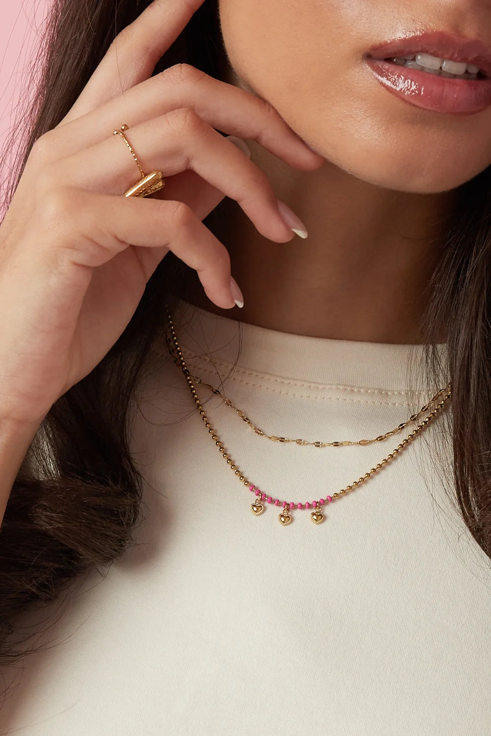 A gold-plated stainless steel multi-layer necklace featuring a top tier textured gold chain and a bottom tier gold satellite chain decorated with hot pink seed beads and three small hanging heart charms. mimi-multi-layer-heart-fringe-necklace.webp