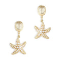 A pair of gold-plated drop earrings by Bill Skinner featuring a ribbed scallop seashell stud suspending a three-dimensional starfish encrusted with smooth white faux pearls.