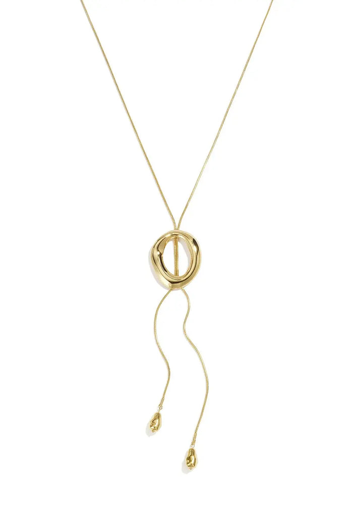 A gold-plated stainless steel lariat necklace featuring a fluid snake chain passing through a sculpted molten oval ring with two cascading chain ends finished with organic teardrop beads against a white background. paloma-molten-ring-lariat-teardrop-necklace.webp