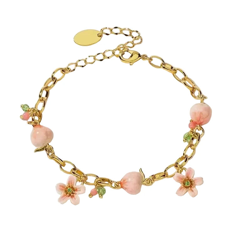 A gold link chain charm bracelet decorated with hand-painted pink enamel peaches, pink flower charms with green crystals, and tiny pink and green beads on a white background.