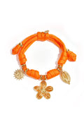 A vibrant orange braided cord bracelet featuring gold charms of a flower, a sun, and a cowrie shell, displayed on a white background.
