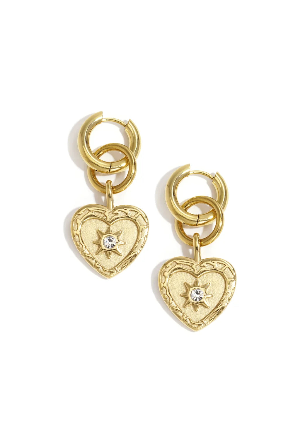 A pair of gold-plated stainless steel huggie hoop earrings featuring a cascading drop of a secondary ring and a textured baroque heart medallion coin with an engraved starburst and a tiny clear cubic zirconia center against a white background. stella-celestial-heart-medallion-huggie-earrings.webp