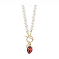 A faux pearl strand necklace by Bill Skinner featuring a front gold-plated toggle clasp suspending a hand-painted 3D red strawberry charm and a small white flower charm.